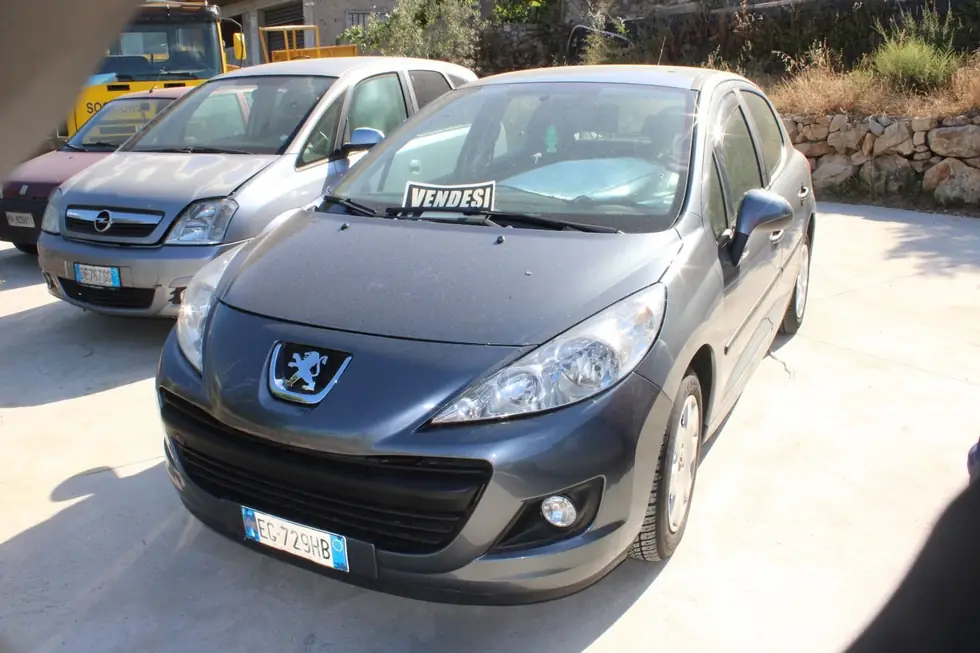Peugeot 207 grigia con il cartello VENDESI davanti ad altre auto nel piazzale
